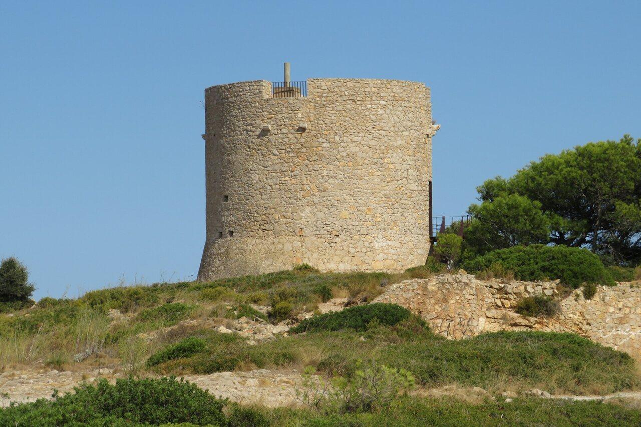 Round stone watchtower standing on the dry scrub-covered headland above Montgó